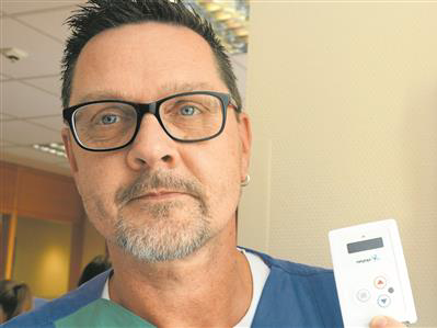 A man is holding an RTLS tag in his hand, with a wall-mounted charging station containing additional tags in the background.